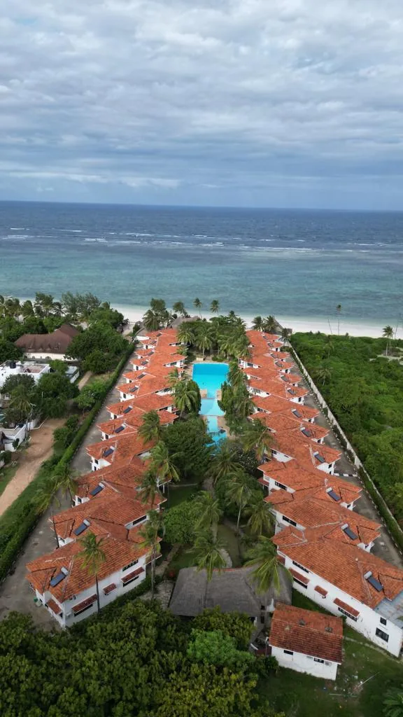 Vue aérienne verticale du resort : villas aux toits de tuiles orange de part et d'autre de la piscine, face à la mer